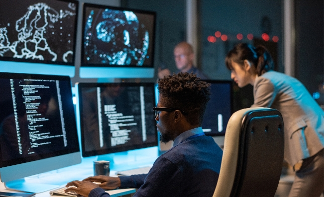 Professionals working at a hi-tech control room with multiple computer monitors displaying data and maps.